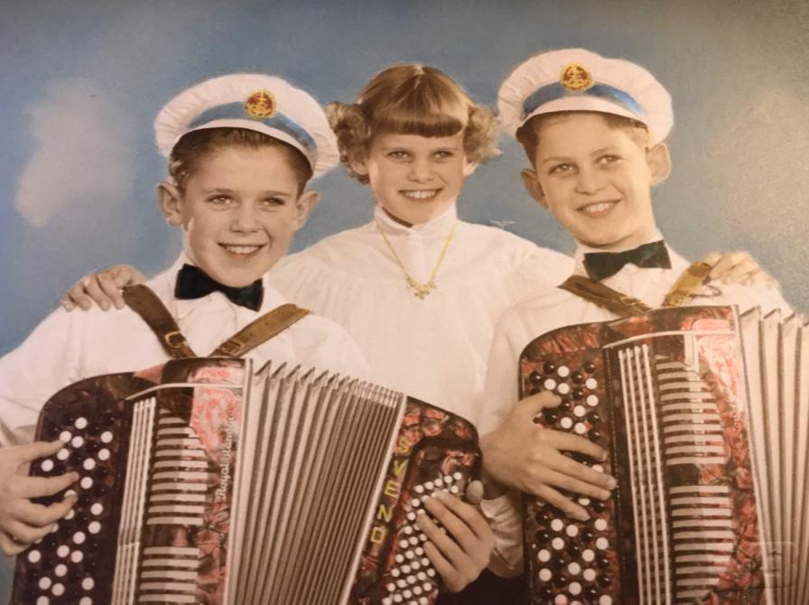 Farvefoto/collage af børnetrioen Svend, Inge og Knud fra Hørve. To drenge med kaptajshatte, der spiller harmonika og en pige i midten med en hånd på hver deres skulder.