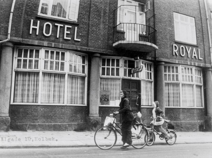 Sort-hvid foto: Hotel Royals facade i 1975. Kvinde og barn cykler forbi.