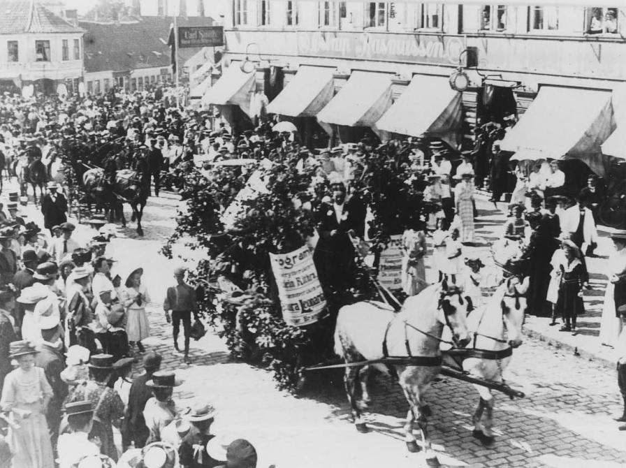 Sort-hvid foto: Her ses de blomsterudsmykkede vogne i optog på vej op ad Ahlgade til Børnehjælpsdagen i juni 1910. Store menneskemængder.